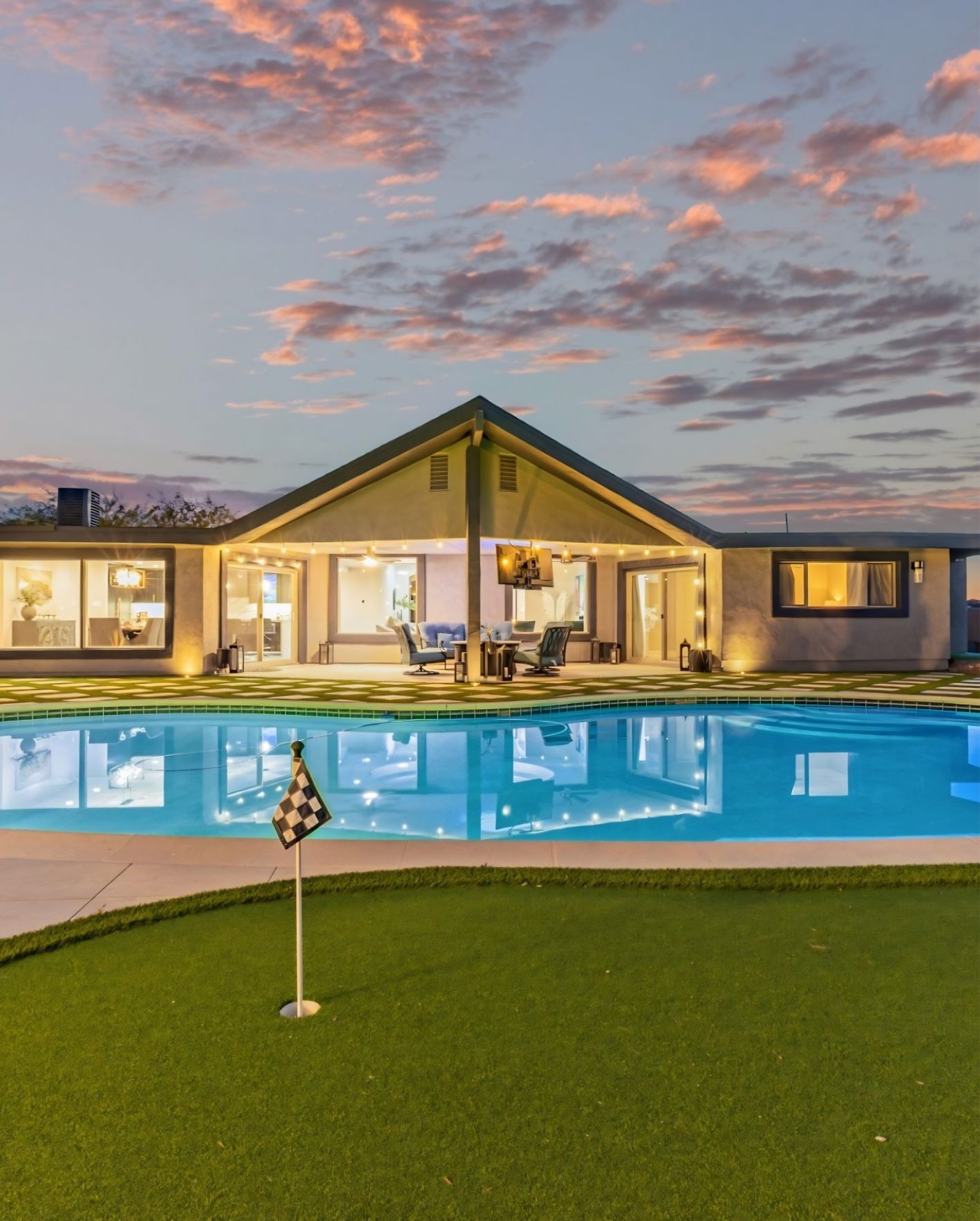 Modern Orlando short-term rental home with a lit patio, swimming pool, and backyard putting green at sunset.