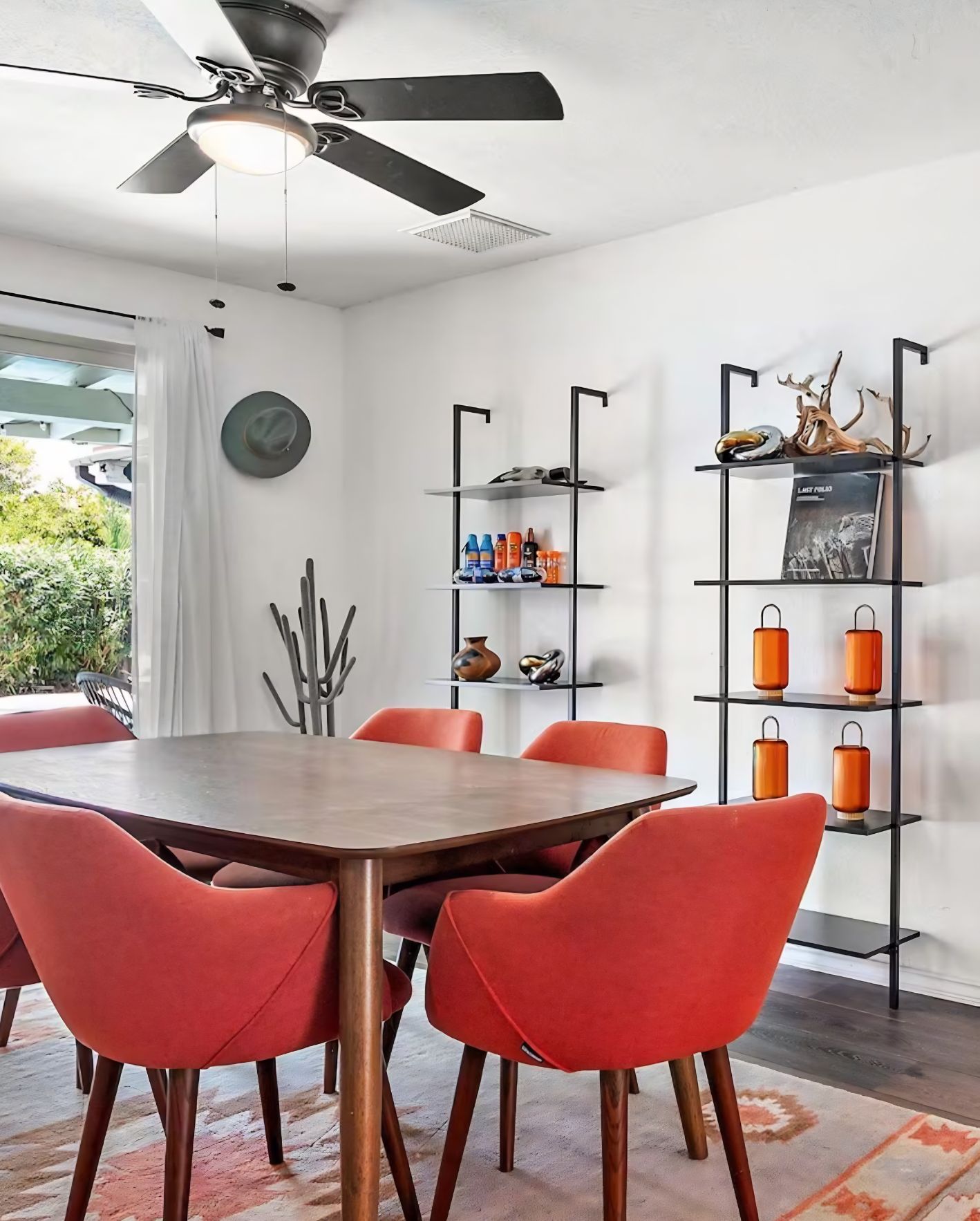 Staged Orlando Airbnb dining area with orange chairs, modern shelving, ceiling fan, and natural light from the patio.