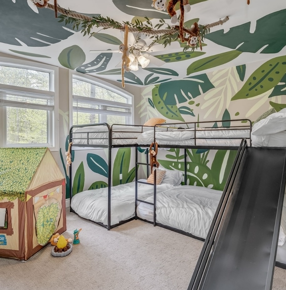 Jungle-themed Airbnb kids’ bedroom with mural walls, bunk bed with slide, hanging monkey toys, play tent, and large windows.