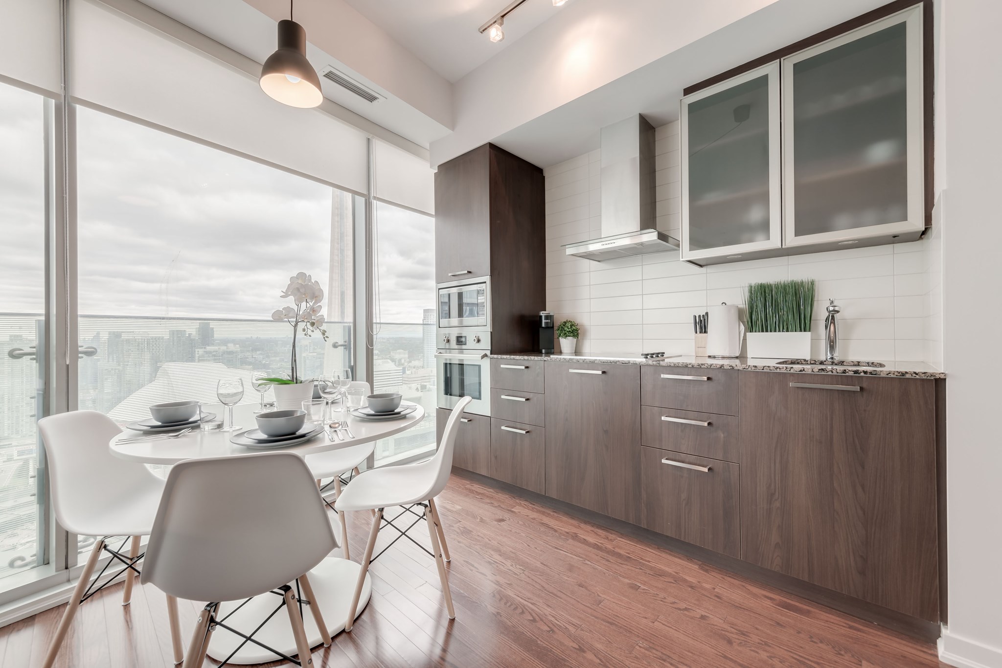Modern Airbnb kitchen and dining area with floor-to-ceiling windows, city skyline views, wood cabinetry, and a staged four-seat dining table.